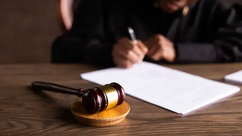 A judge's desk with the focus on the gavel, and the judge signing papers in the background