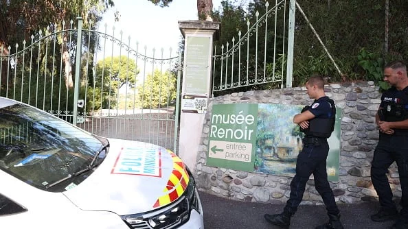 Police officers stand outside a gate near a sign that says Renoir Museum in French.